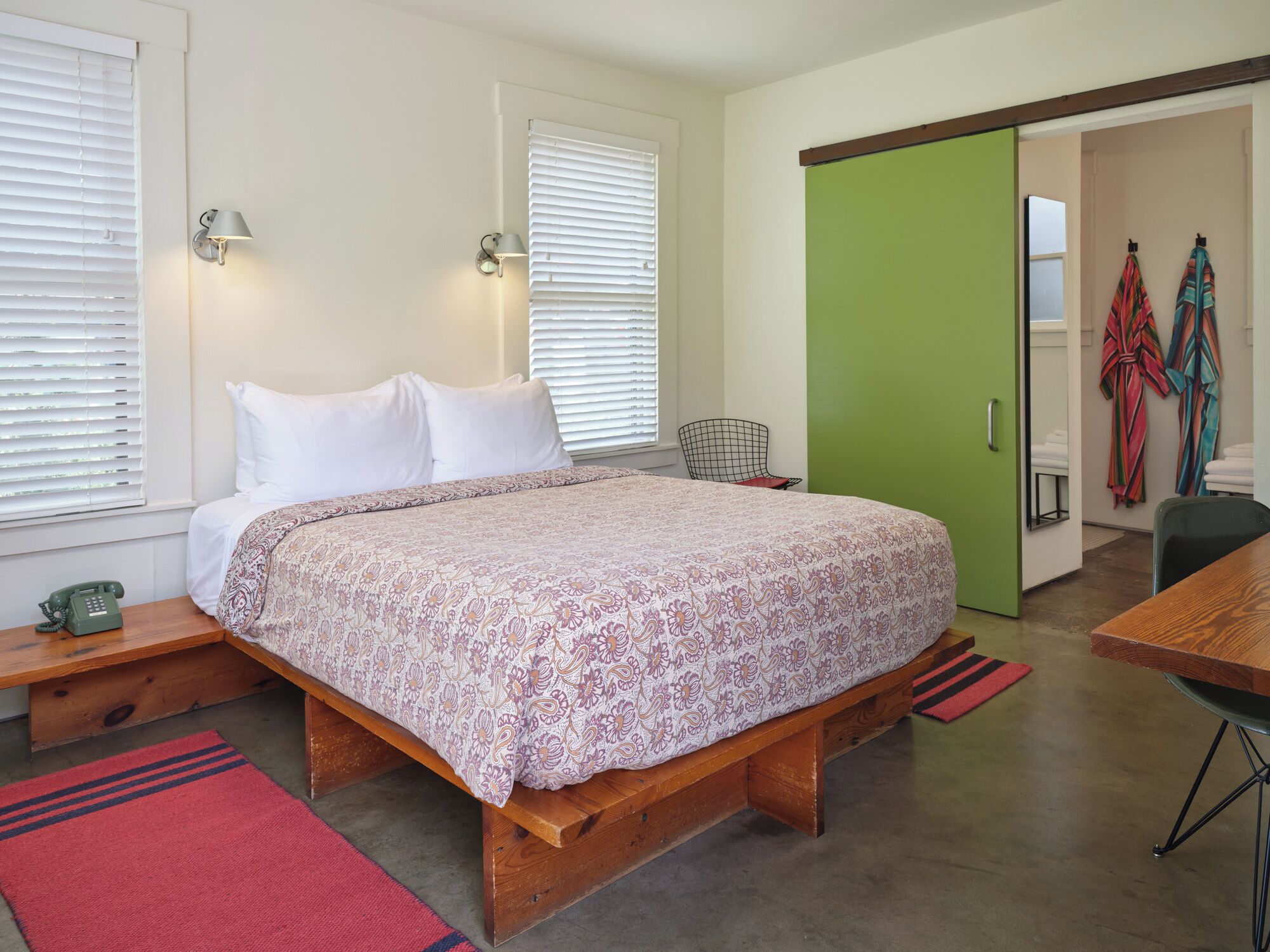 A bedroom with a wooden bed, two bedside tables, a green door, and a chair.