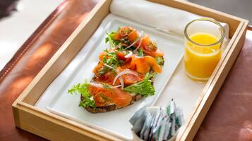 A breakfast tray with smoked salmon on toast, a glass of orange juice, and a small container of condiments.