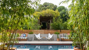 A poolside area with a wooden deck, two white chairs, a sofa with colorful cushions, and potted plants. - Hotel San Jose (Austin)