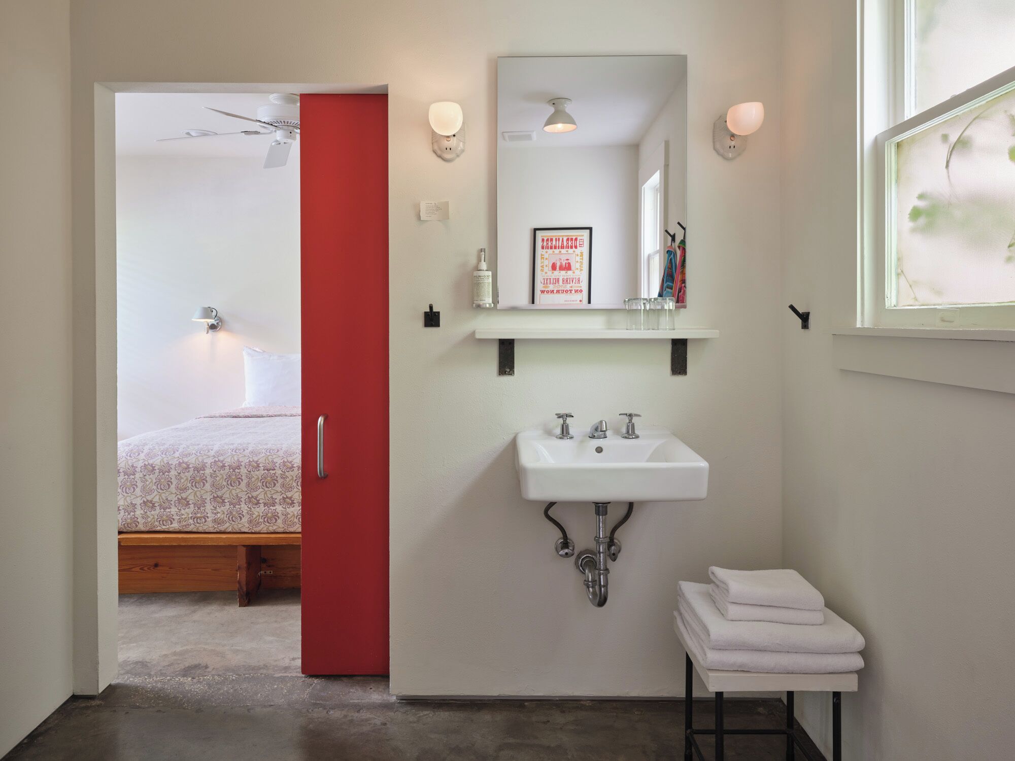 A bathroom with a white sink, a mirror, and a red door leading to a bedroom.