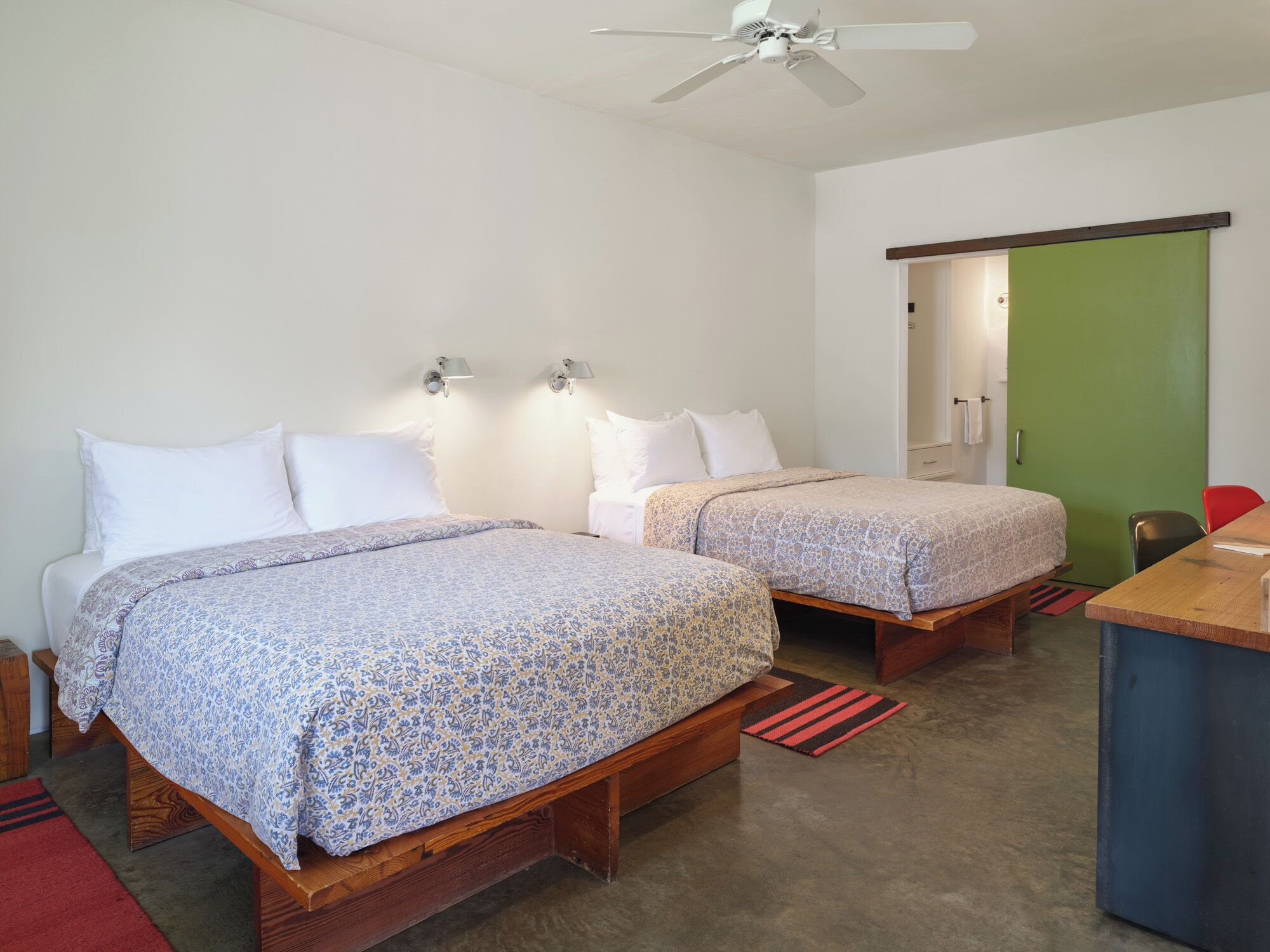 A room with two wooden beds, a ceiling fan, a green door, and a small table.