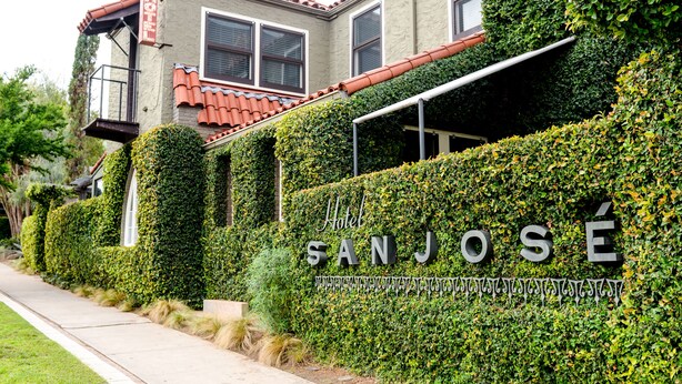 A hotel named "Hotel SANJOSÉ" with a red-tiled roof, a balcony, and a well-maintained hedge. - Hotel San Jose (Austin)