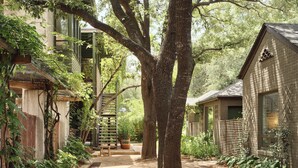 A pathway flanked by trees and buildings, with a wooden staircase leading to a covered area. - Hotel San Jose (Austin)