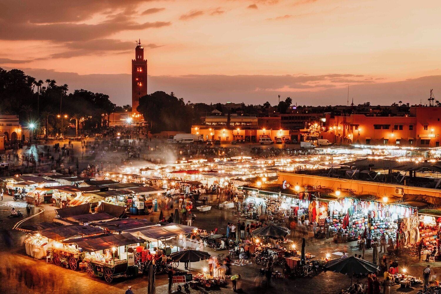 A bustling nighttime market with numerous stalls and a prominent tower in the background.