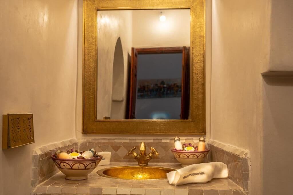 Un baño con un lavamanos dorado, dos cuencos con artículos de tocador y un espejo con marco dorado.