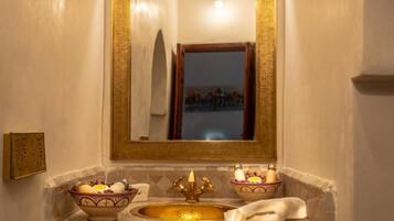 Un baño con un lavamanos dorado, dos cuencos con artículos de tocador y un espejo con marco dorado.