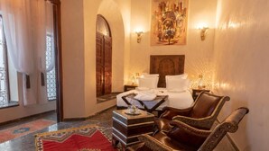 A traditional room with a bed, a leather armchair, a small table, and a red patterned rug. - Palais Aix Kabaj & Spa (Marrakech)