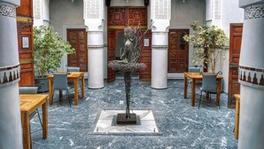 A courtyard with marble flooring, wooden tables, chairs, and a central sculpture. - Palais Aix Kabaj & Spa (Marrakech)