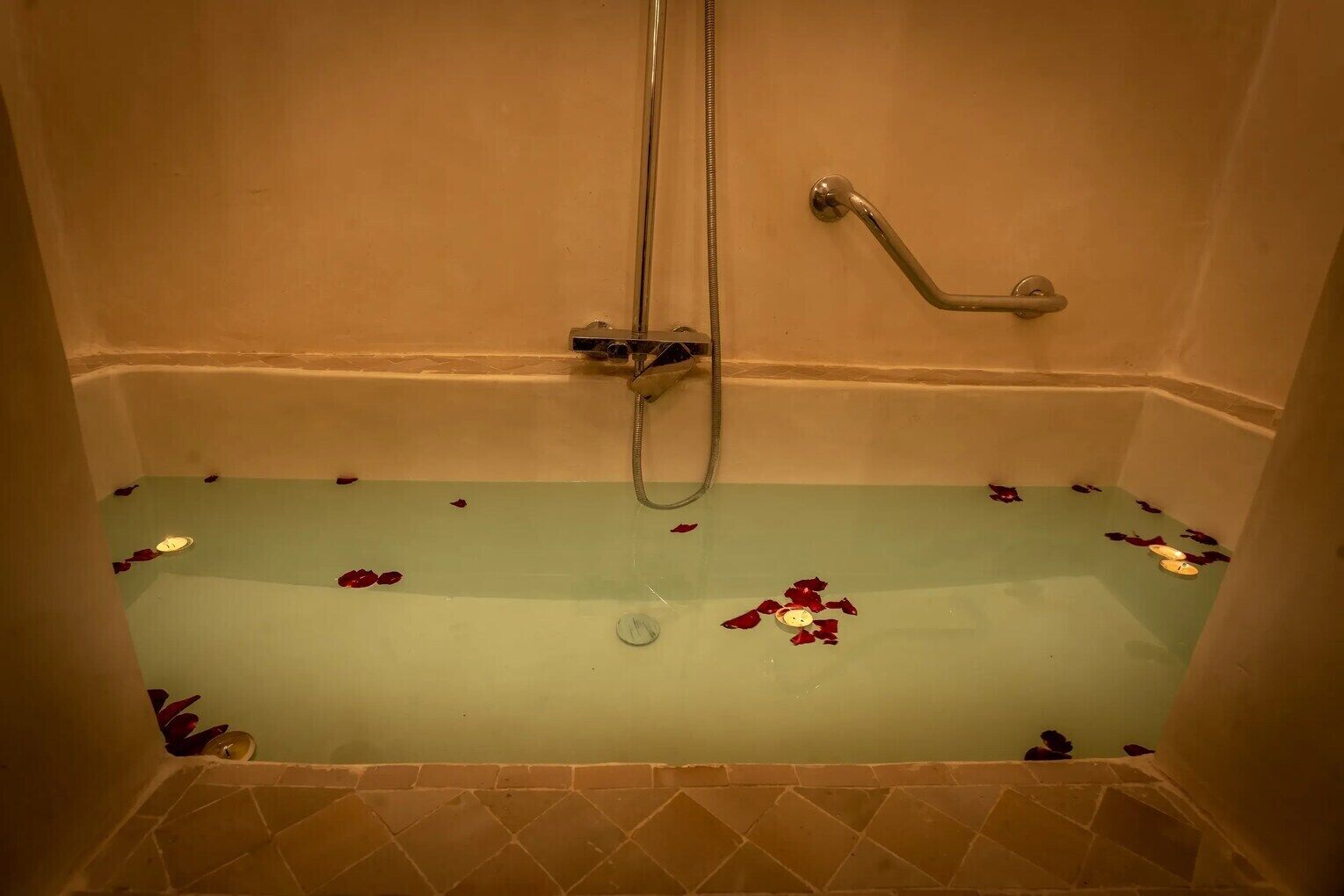 A bathtub with rose petals, a handheld showerhead, and a wall-mounted faucet.