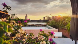 A rooftop terrace with a table and chairs, surrounded by lush greenery and a view of a distant tower. - Palais Aix Kabaj & Spa (Marrakech)