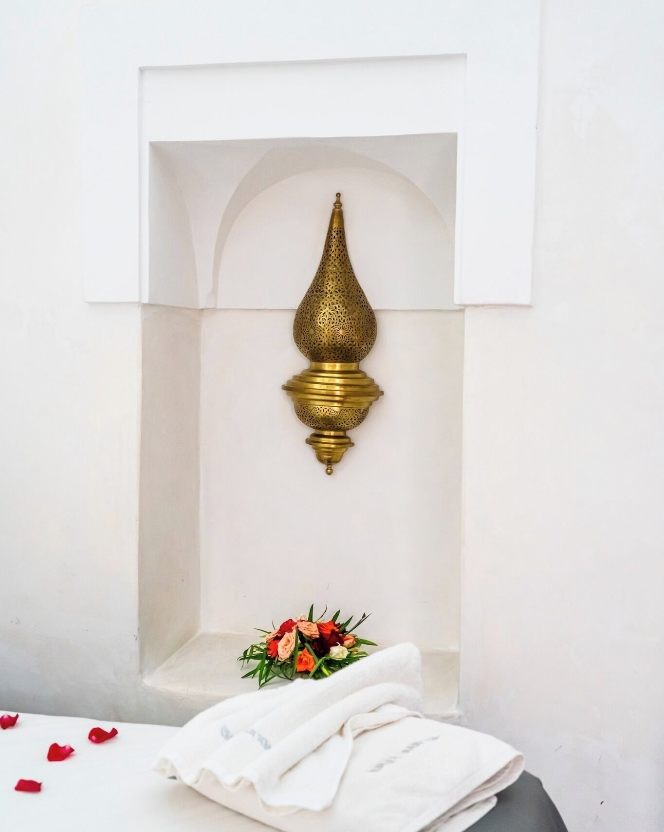A white wall with a decorative brass fixture and a small table with a bouquet of flowers and a folded white cloth.