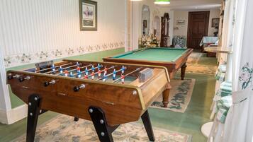 Een pooltafel met een tafelvoetbal in een kamer met gestreept behang, een kroonluchter en een bloemenprint tapijt.