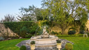 A garden with a fountain, stone wall, and greenery. - Homerez - House in Saint-Martin-des-Entrées (Saint-Martin-des-Entrées)