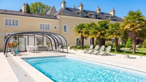 A swimming pool with lounge chairs, a covered seating area, and a building with a tiled roof in the background. - Homerez - House in Saint-Martin-des-Entrées (Saint-Martin-des-Entrées)
