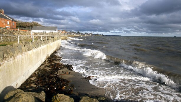 A coastal scene with a stone wall, waves, and buildings in the background. - Coastguard Boat House on Belfast Lough (Newtownabbey)
