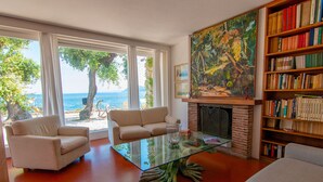 A living room with a fireplace, a bookshelf, and a view of the sea. - Villa Le Grotte on the sea Elba Island (Portoferraio)