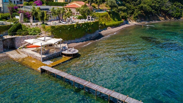 A coastal area with a wooden pier extending into clear blue water, a stone wall, and a building with a red roof. - Villa Le Grotte on the sea Elba Island (Portoferraio)