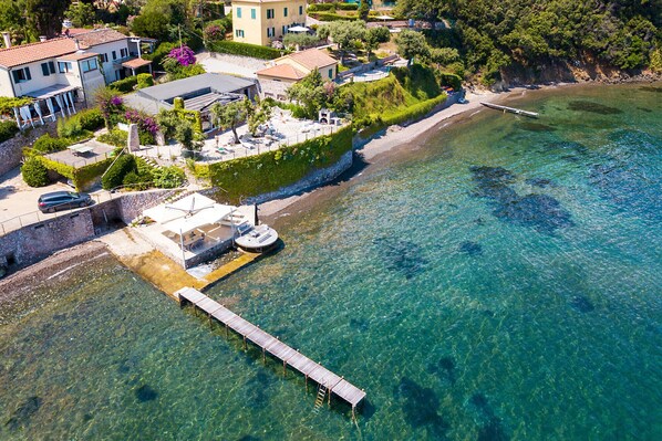 An aerial view of a coastal property with a clear waterfront, a dock, and a small boat.