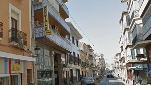 Una vista di strada con una fila di edifici, tra cui un albergo chiamato "HOSTAL R" con una segnaletica che indica una direzione.