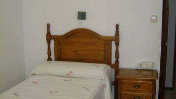 A single bed with a wooden headboard, a nightstand with a lamp, and a small dresser.