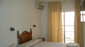 Camera da letto con un letto in legno, un comodino, un condizionatore d'aria a parete e vista su un balcone esterno.