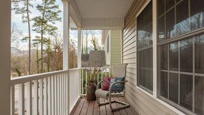 Une véranda en bois avec une balustrade blanche, une chaise berçante et une grande fenêtre.