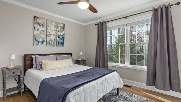 Une chambre à coucher avec un lit, un ventilateur de plafond, une fenêtre avec des rideaux et des œuvres d’art accrochées au mur.