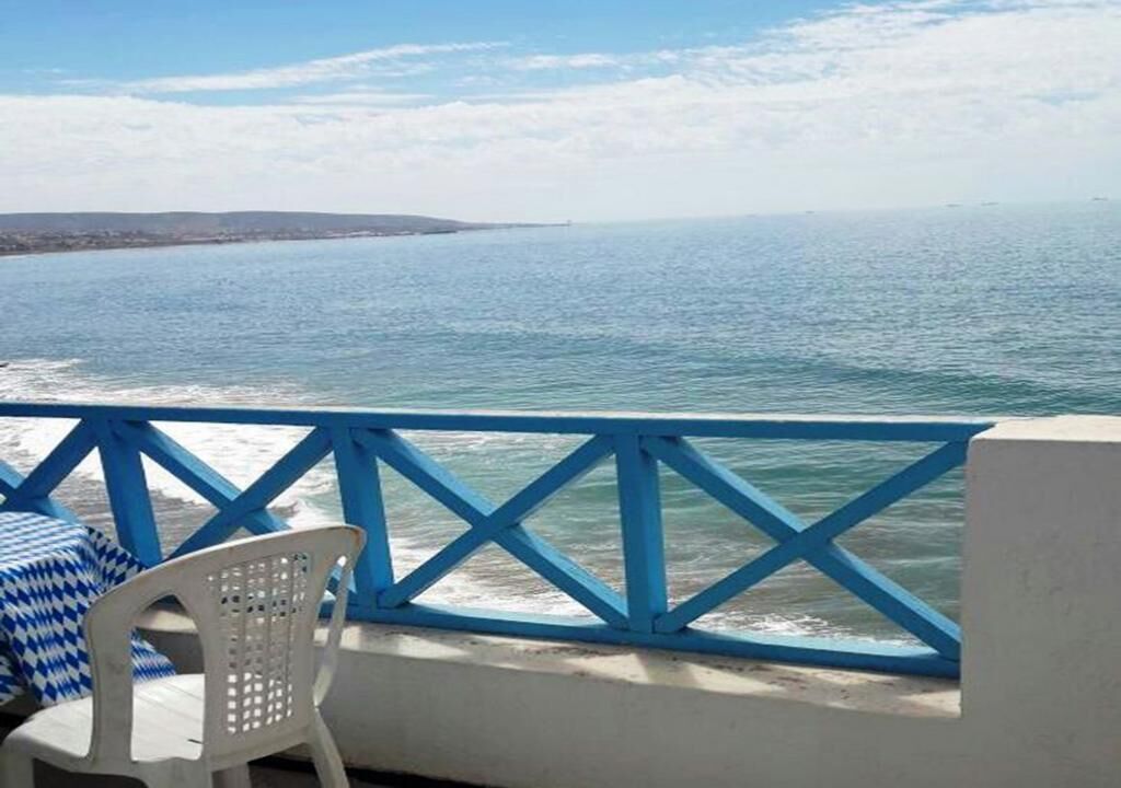 Un balcón con vista al mar, una silla de plástico blanca y una barandilla azul.