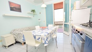 Un coin repas avec une table dressée pour quatre personnes, un canapé et un espace cuisine équipé d’un réfrigérateur et d’une cuisinière.