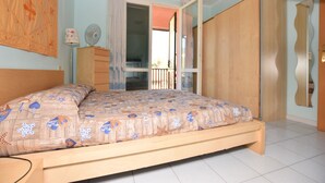 Une chambre avec un lit en bois, une commode, un ventilateur et une vue sur l’extérieur.