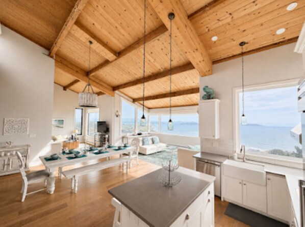A spacious kitchen with wooden beams, a dining area with a view, and a large window overlooking the sea.