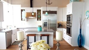 A modern kitchen with white cabinets, stainless steel appliances, and a central island with stools. - KH: Life is a Beach (Dillon Beach)
