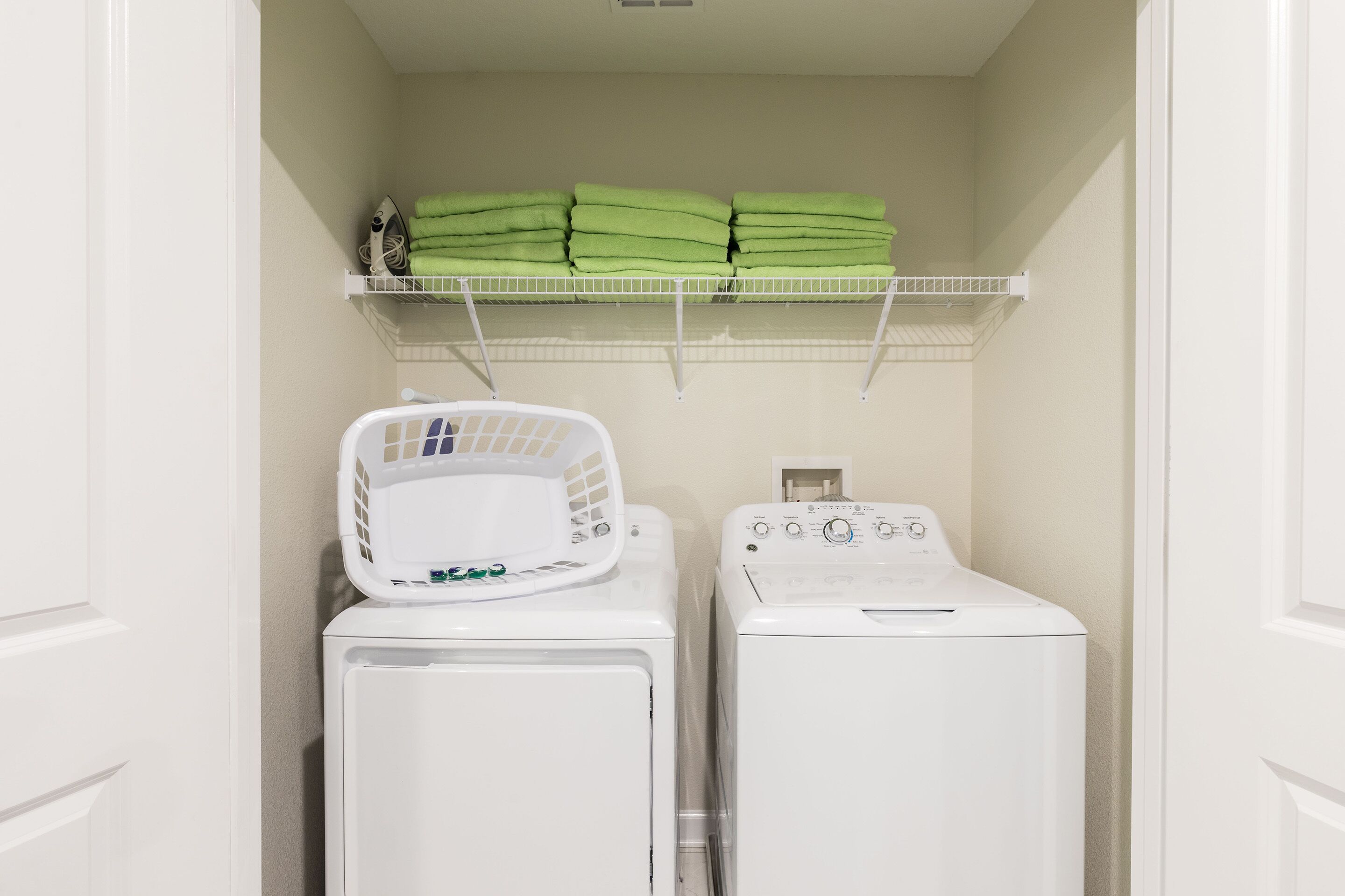 A laundry room with a stacked drying rack, a washing machine, and a shelf with folded towels.
