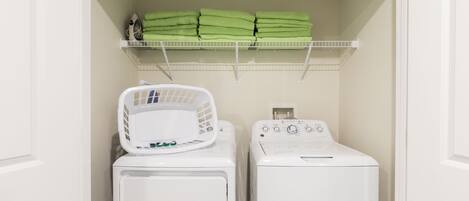 A laundry room with a stacked drying rack, a washing machine, and a shelf with folded towels.