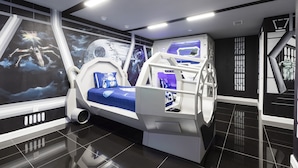 Una habitación futurista con cama, escritorio y un mural de espacio en la pared.