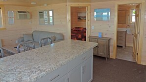 Interior d'una cabana amb zona de cuina, taula de menjador i sofà.