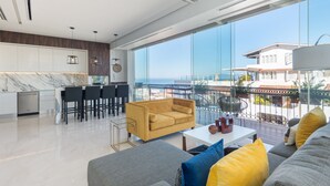 A modern living room with a sofa, a coffee table, and a dining area with chairs and a table. There is a large window with a view of the sea and buildings. - Bright Pier57 Corner Unit Ocean View Romantic Zone (Emiliano Zapata)