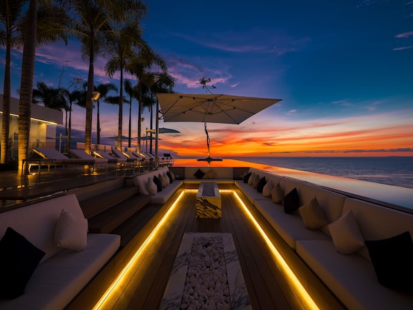 Un espacio exterior lujoso con vistas al atardecer, sofás blancos acolchados y una terraza de madera.