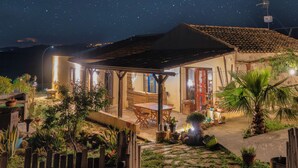 A cozy outdoor patio area with a wooden table and chairs, surrounded by potted plants and a palm tree. - B&B Polvere Di Stelle (Trapani)