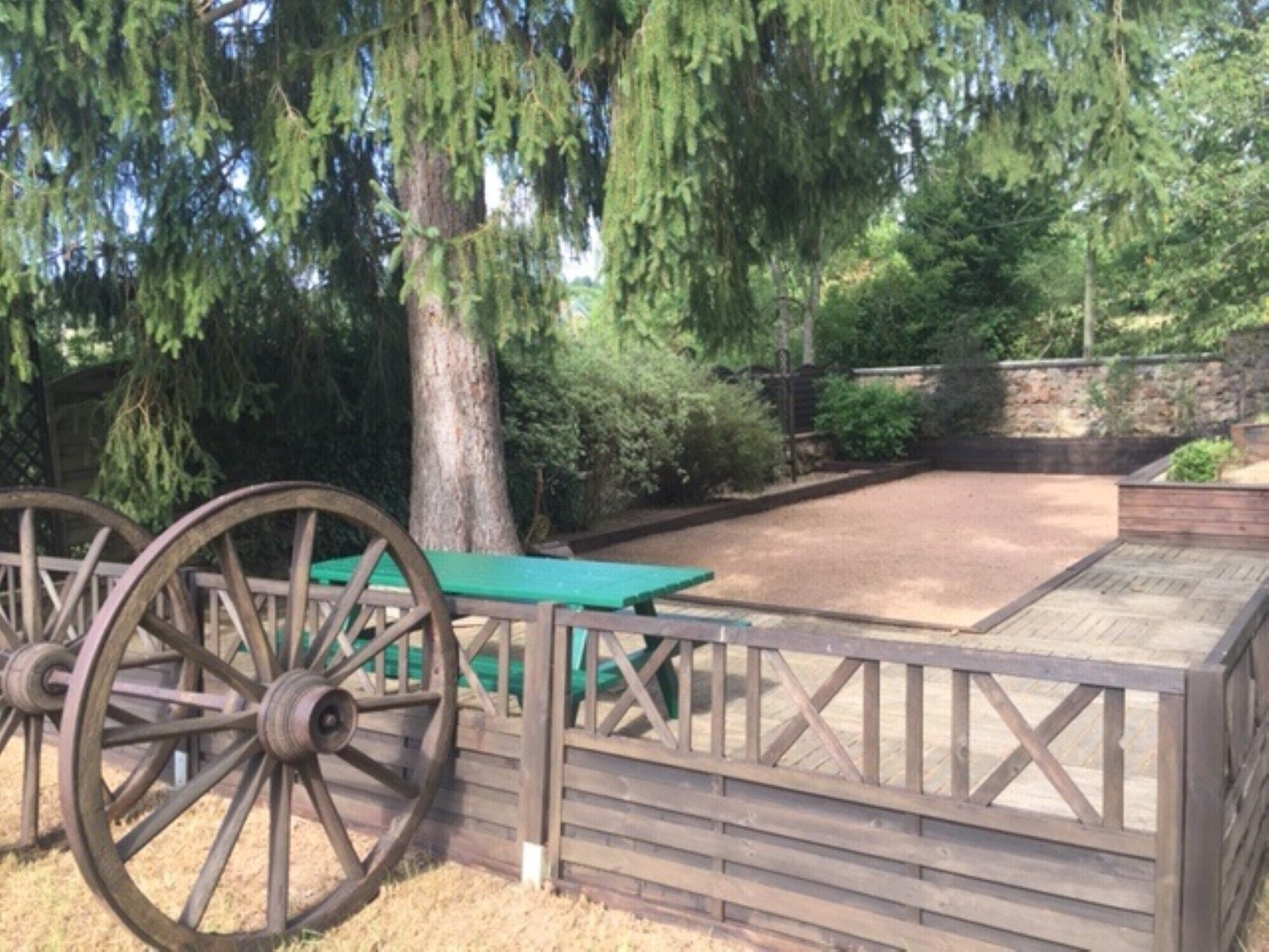A rustic outdoor area with a wooden fence, a green picnic table, and a large wooden wheel structure.