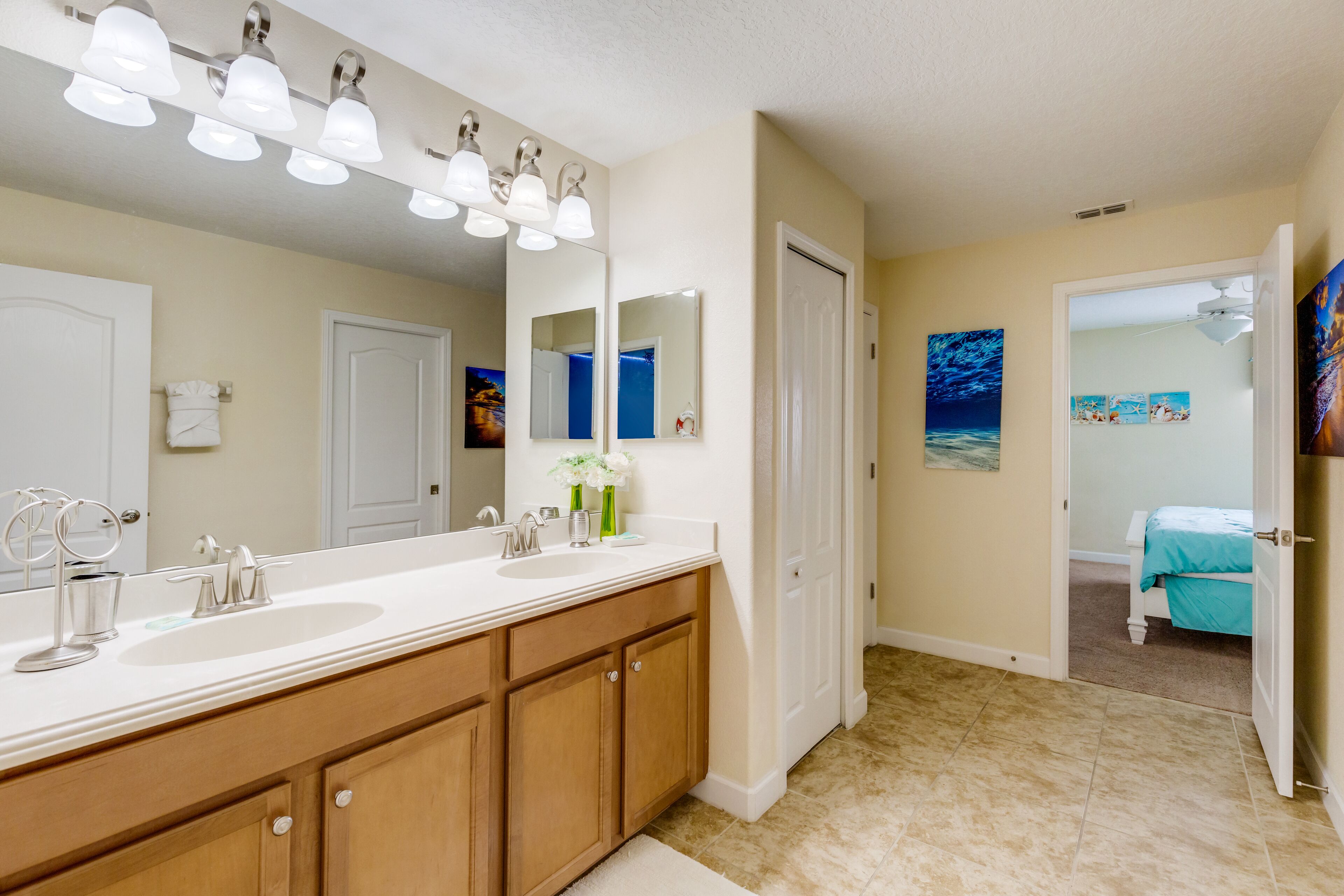 A bathroom with a double sink vanity, a large mirror, and a door leading to a bedroom.
