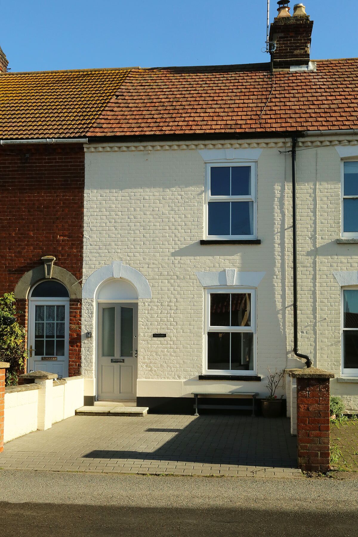 A two-story building with a red-tiled roof, white brick walls, and a central entrance with a white door and windows.