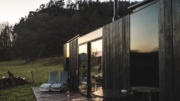Una terraza moderna al aire libre con sillones de descanso y una mesa, con vistas a un área verde y una colina boscosa.