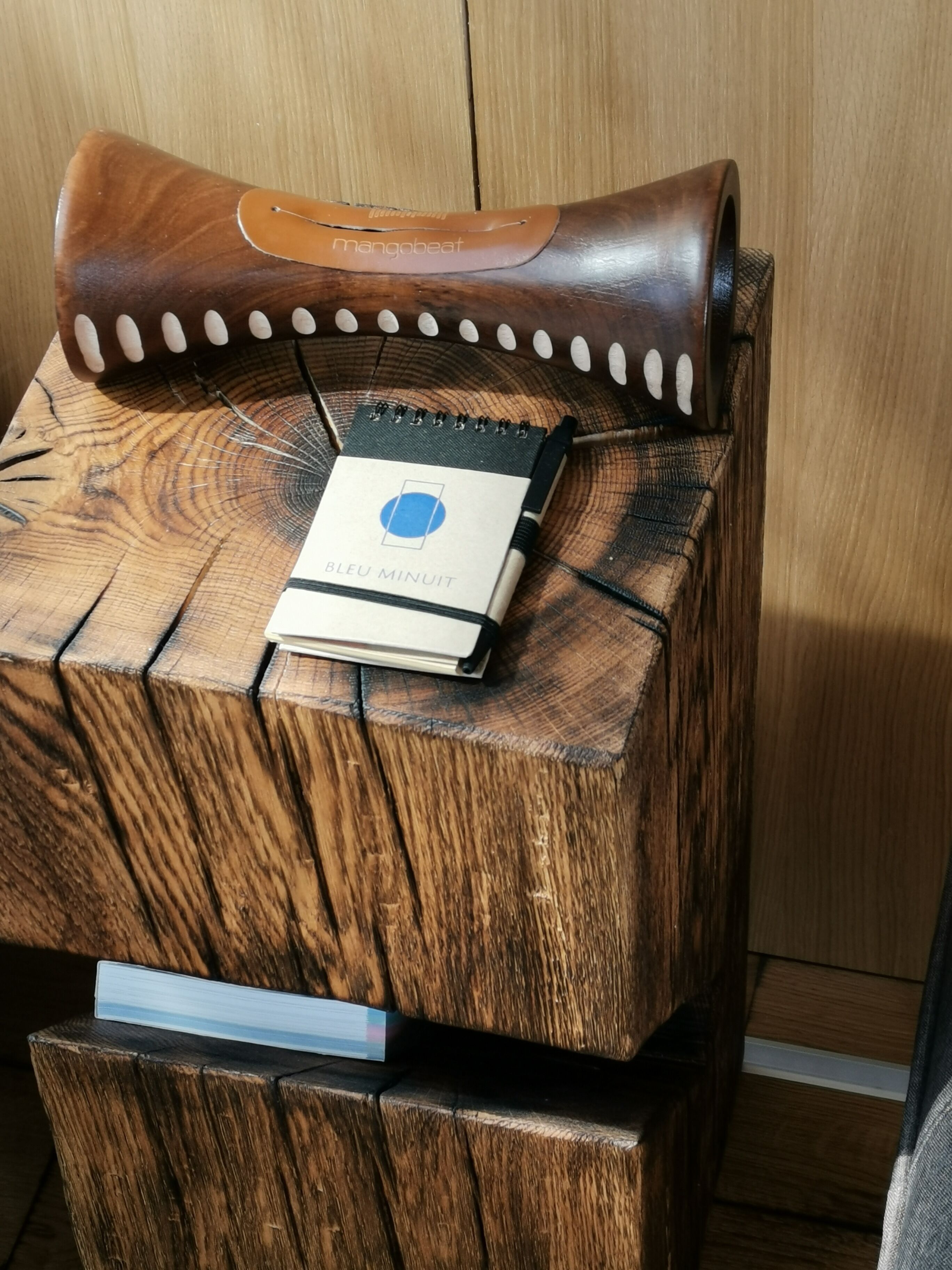 A wooden chair with a leather backrest and a notebook labeled "Bagu Minuit" on a wooden surface.