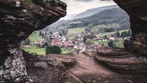Vista a través de un arco de roca con vistas a un pueblo con casas y campos verdes.