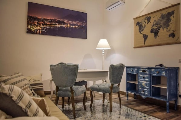 Una sala de estar con sofá, dos sillones, una mesa, una lámpara, un mapa del mundo y un cuadro de un paisaje urbano.