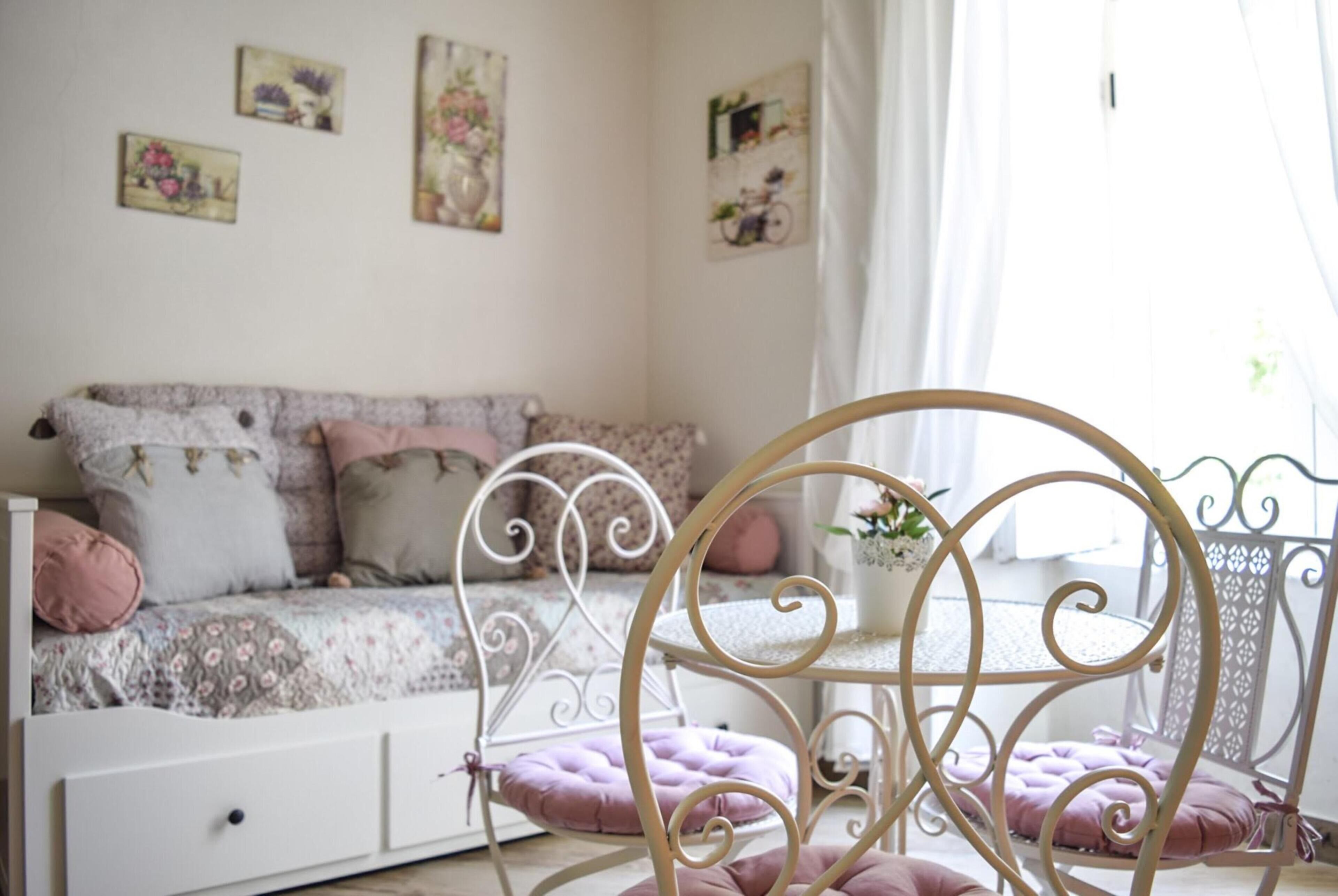 A cozy bedroom with a floral-patterned bed, a white dresser, and a decorative chair with a cushion.