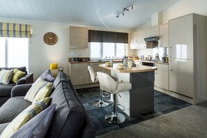 Una cocina moderna con una isla central, un área de comedor con sofá y un amplio ventanal con persianas.