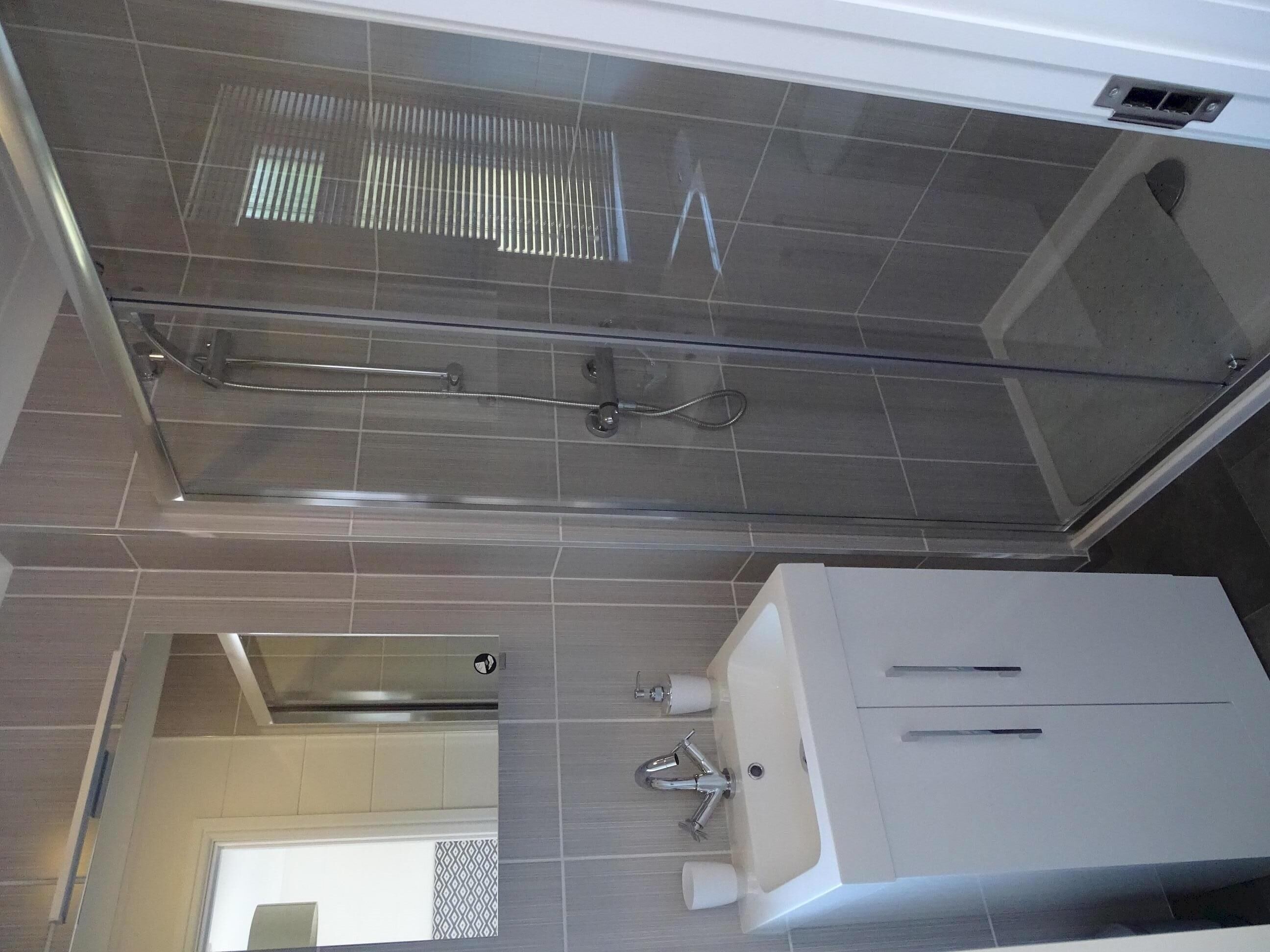Une salle de bain moderne avec une douche à parois de verre, un lavabo blanc avec un robinet et des toilettes.