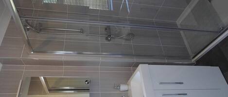 Une salle de bain moderne avec une douche à parois de verre, un lavabo blanc avec un robinet et des toilettes.